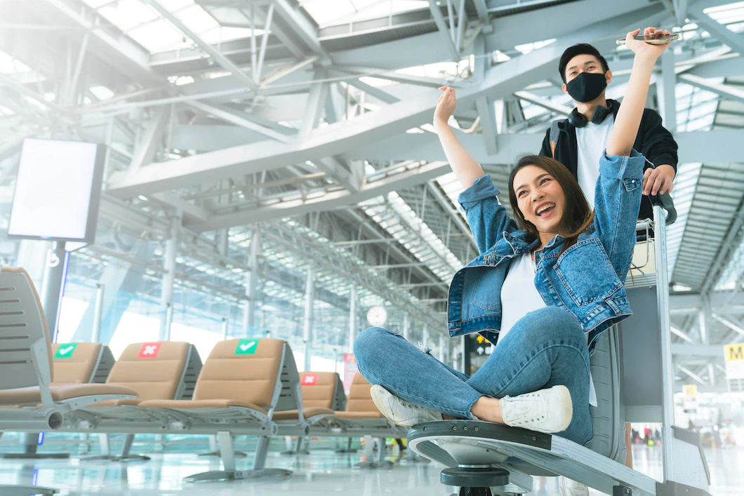 Attractive young asian tourist couple excited together for the trip girlfriend sitting and cheering on baggage trolley